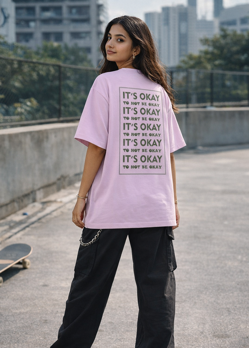 Person wearing a pink t-shirt with text on it, standing on a rooftop with a skateboard and cityscape in the background.