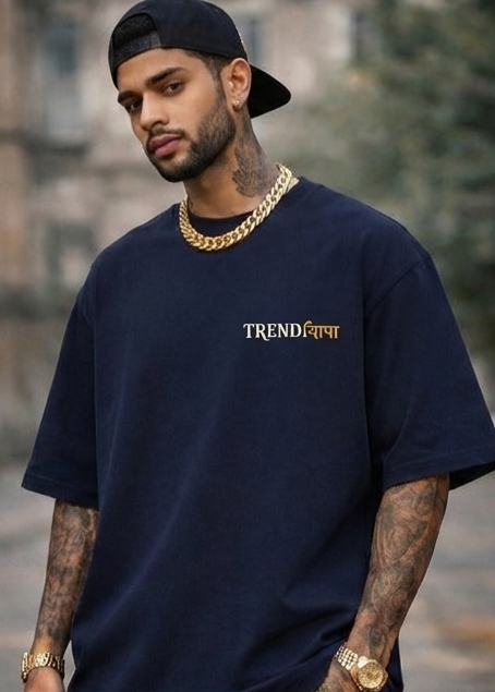 Man wearing a navy blue t-shirt with 'TRENDiyapa' logo, gold chain, and watch outdoors.